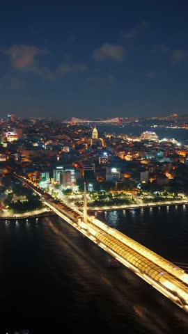 Vertical aerial view of the Istanbul cityscape and bridges over the Bosphorus Strait at night, with illuminated buildings and the Galata Tower visible in the distance