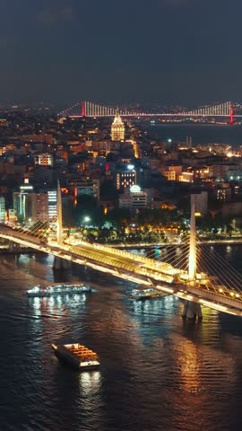 Vertical aerial view of the Istanbul cityscape and bridges over the Bosphorus Strait at night, with illuminated buildings and the Galata Tower visible in the distance