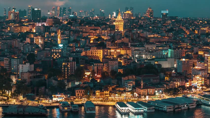 Galata Tower rising above the rooftops of Istanbul's buildings at night, with the cityscape illuminated against the night sky