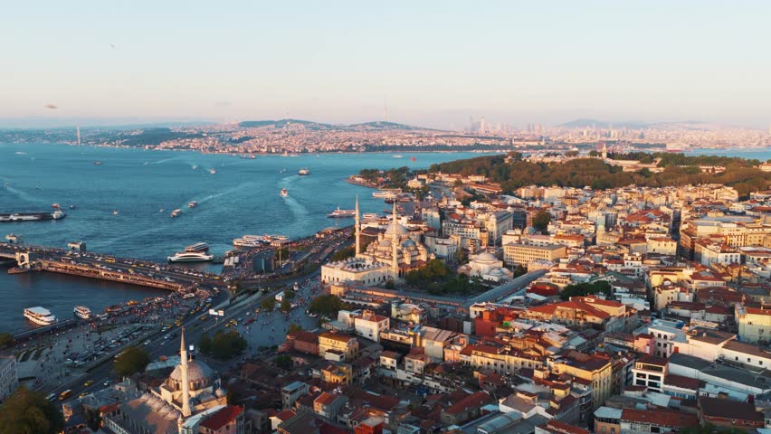 Aerial view of the Galata Bridge and the Golden Horn at sunset, with busy traffic, a mosque in the foreground, and the Bosphorus Strait in the distance