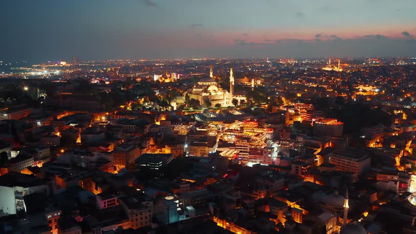 Aerial view of the historic Suleymaniye Mosque and surrounding residential buildings in Istanbul at night, with the cityscape illuminated against the night sky
