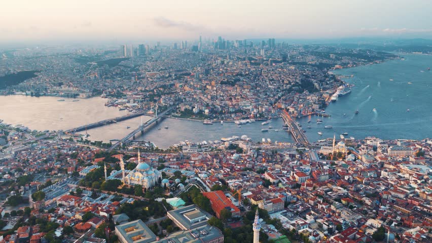 A wide aerial view of the historic Istanbul cityscape, showing the Bosphorus Strait and its bridges, with multiple mosques and buildings in the foreground