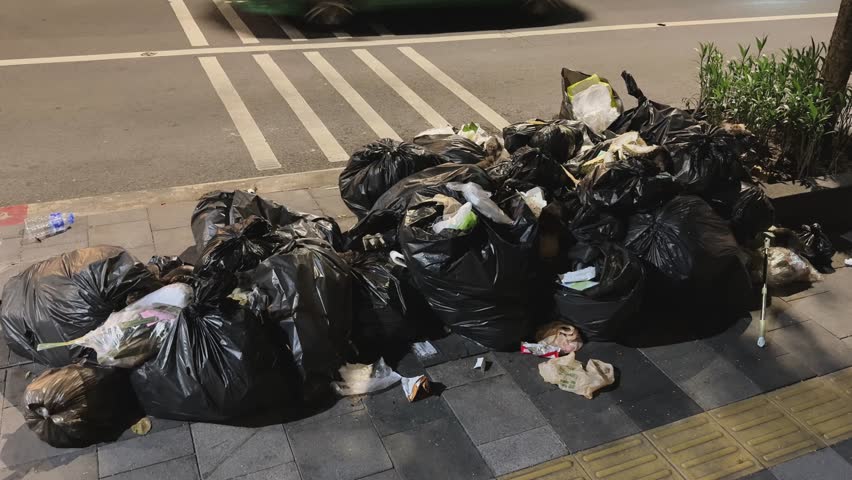 Overflowing black garbage bags with rats scavenging on a night street sidewalk