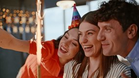 Happy colleagues enjoy birthday celebration office party together closeup. Cheerful young coworkers making selfie at company workplace in bright festive caps. Joyful team holding cake taking picture - Powered by Shutterstock - Get 15% off with code: PIKWIZARD15