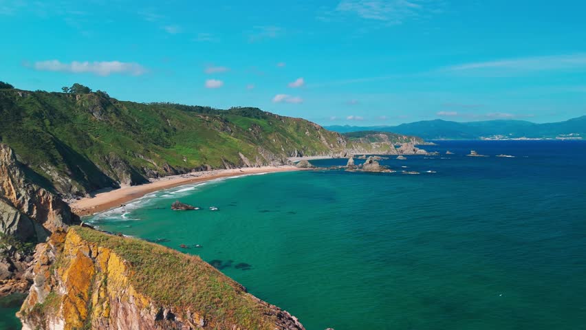 Aerial view of the Atlantic Ocean coast in Galicia, Spain, featuring high cliffs, sandy beach, and turquoise sea. Dramatic natural landscape showcasing rugged coastline and scenic ocean views.