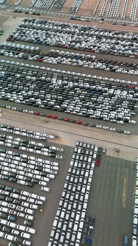 Aerial view of new cars parked in rows at a sea port stock lot. Vehicle inventory for sale, import, and export in the global automotive business. Logistics and distribution hub.
