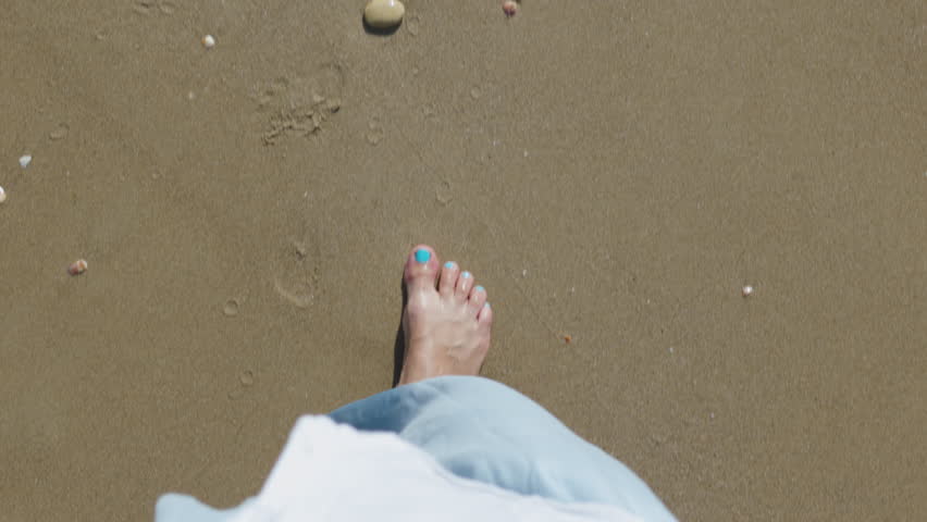 A girl enjoys a barefoot walk on the sand and clear tropical ocean. POV shot, close-up. The joy of walking barefoot in the seawater, the splashes, the happiness. Bare feet in the water.