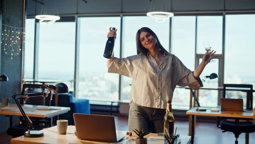 Carefree woman dancing office drinking champagne alone. Relaxed drunk businesswoman celebrating success enjoying moment in empty corporate workplace. Happy lady manager holding alcohol bottle swinging