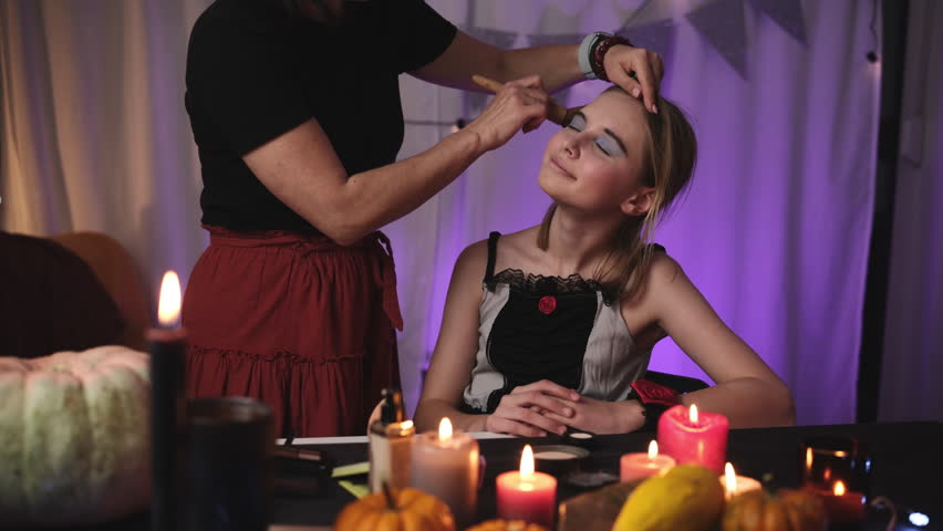 Mom Applying Spooky Halloween Makeup To Daughter In A Decorated Room