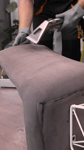 Male worker dry cleaner removing dirt from armchair with vacuum cleaner