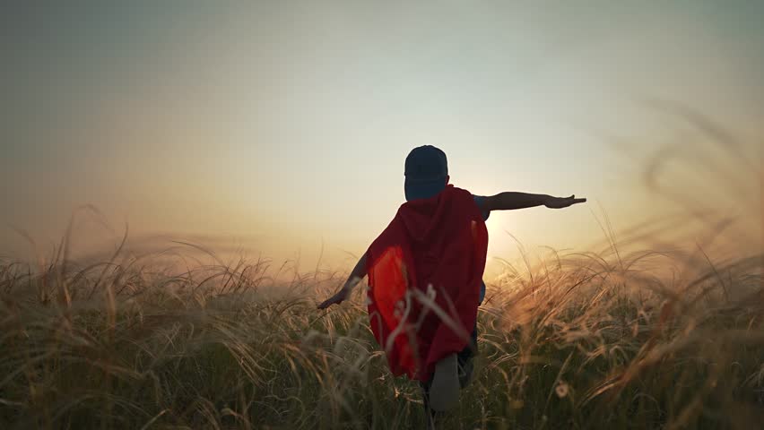 This kid spreads his arms like a superhero, the cape flying in nature. The boy runs through the field, full of freedom, full of dreams. The child loves the sunset, red skies, and being a fearless boy.