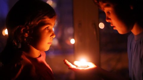 Cute boy and adorable girl stay face to face with a candle and talk