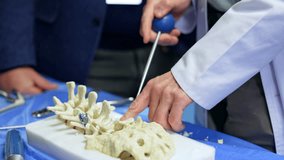 Male hands in white robe applies a tool at the model of spine. Neurosurgery professional is displaying modern instruments application on practice. Close up. - Powered by Shutterstock - Get 15% off with code: PIKWIZARD15