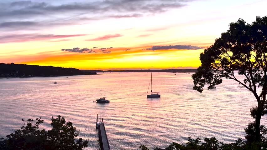 Sunset in Centerport Harbor Long Island with Orange and Yellow Light in the sky and a pink reflection in the water with Moored boat