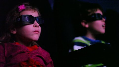 Two kids in cinema watching a 3D movie, focus on girl