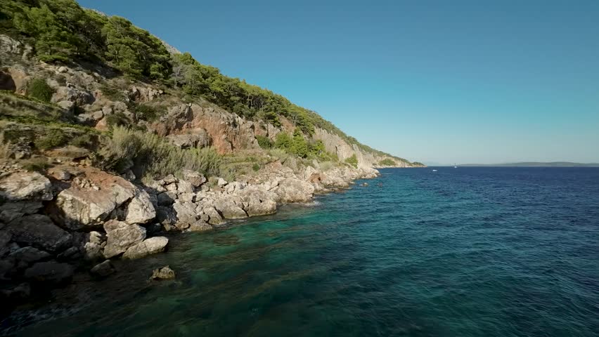 Cinematic FPV drone video flying over rocky coastline and turquoise sea near Sveta Nedelja, Hvar island, Croatia. Clear sky and pine trees.