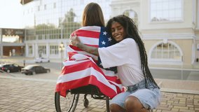 two female multiracial friends one inclusive woman in a wheelchair enjoying a sunny day in the city, celebrating freedom and friendship with an American flag - Powered by Shutterstock - Get 15% off with code: PIKWIZARD15