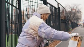 Caucasian woman stands outdoors on a cold autumn day in a town street engaged in artistic creativity. She holds a paintbrush and thinks what to draw on a paper. Practicing craft with portable art kit. - Powered by Shutterstock - Get 15% off with code: PIKWIZARD15