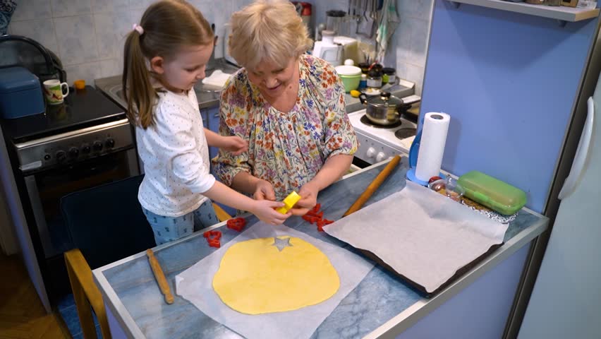 Grandmother and cute little granddaughter making cookies together at home 
