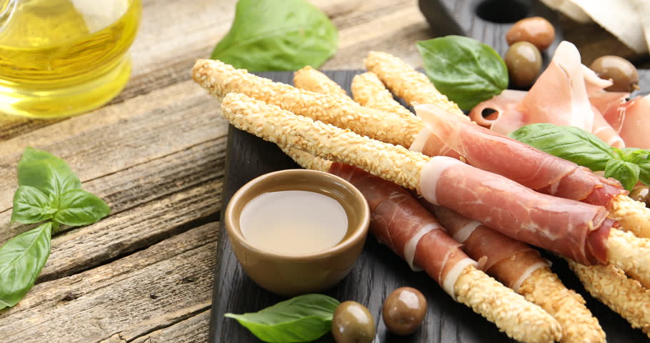 Grissini breadsticks with prosciutto, olives and honey on wooden table, spinning