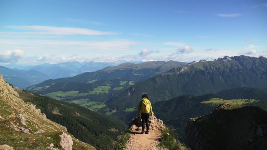 Hiker sitting on rocky trail with panoramic Dolomites mountain valleys in Italy