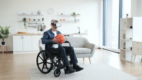 Senior man sitting in wheelchair indoors wears VR headset holding basketball, enjoying technology. Interior setting includes sofa, shelves. Emphasizes virtual reality, accessibility - Powered by Shutterstock - Get 15% off with code: PIKWIZARD15