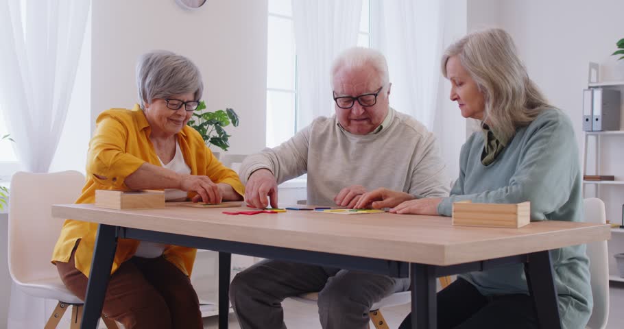 Senior people in the retirement home playing a brain game together. Group of three old friends sitting around a table and solving a shape puzzle. Dementia treatment concept