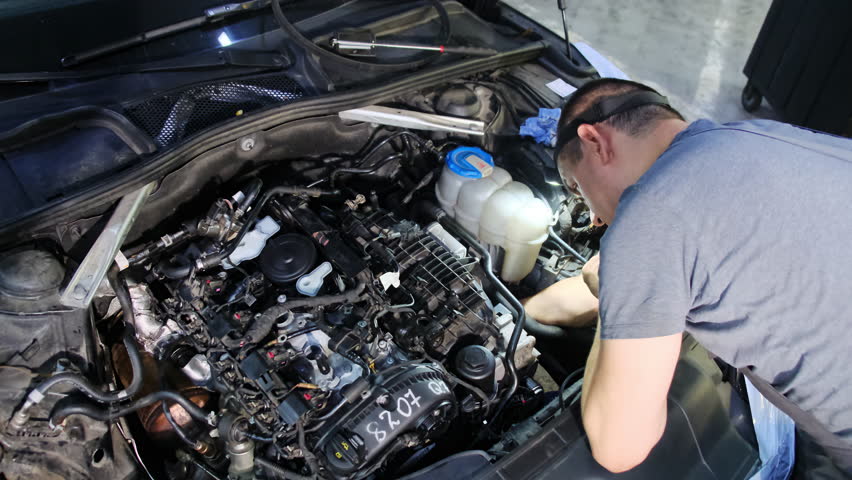 Technician with headlamp inspects engine compartment. Man assesses condition of system and adjusts components to eliminate malfunctions