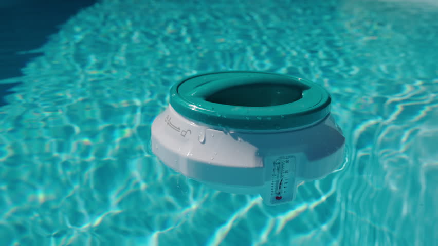 Round pool chlorinator floating on clear blue water with sunlight reflections. High quality 4k footage