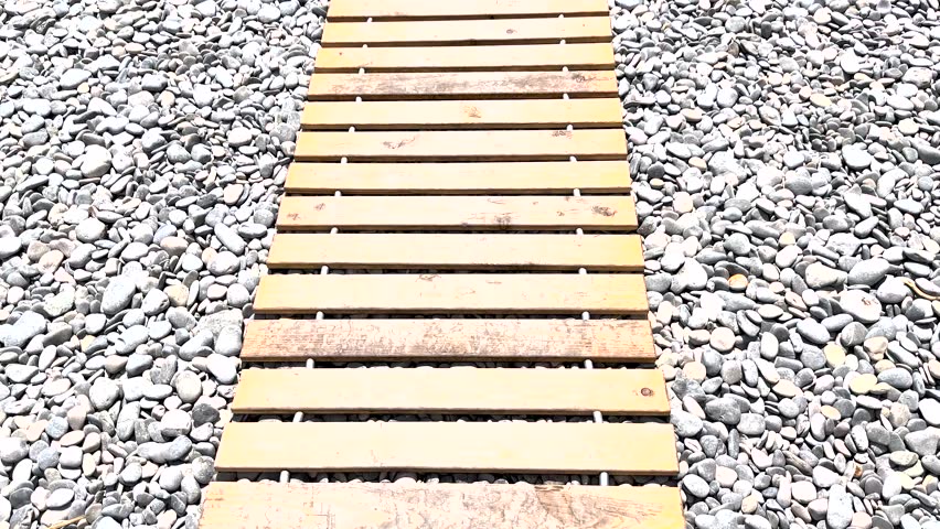Wooden Walkway Leading Through Pebbles on a Sunny Day by the Shore