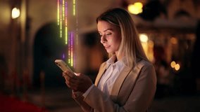 Young woman in business attire using smartphone at night with colorful holographic data streams, futuristic digital overlay. Visualization of Information Lines Flying from Mobile Phone - Powered by Shutterstock - Get 15% off with code: PIKWIZARD15