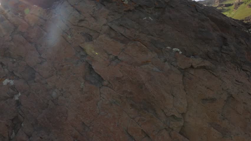 A majestic waterfall cascades down towering mountains, feeding a rushing stream through a lush green valley. Wildflowers adorn rocky slopes, crafting a tranquil natural landscape.