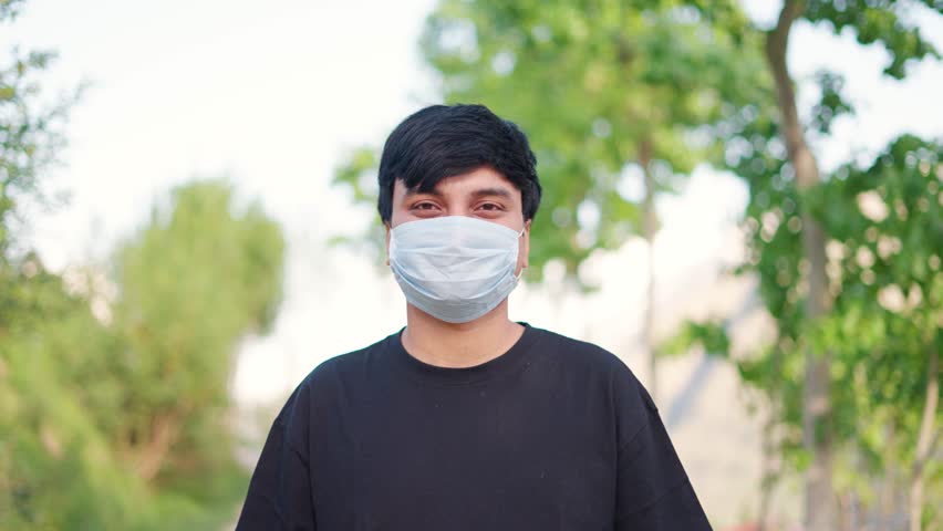 4K Portrait shot of an Indian man wearing face mask showing V sign for peace while standing outdoors. Man shows Peace sign while standing outdoors. Peace and Harmony background with copy space.