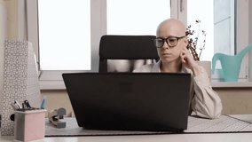 Cancer survivor with bald head and glasses focused on laptop, strong independent woman working remotely from home office with plants - Powered by Shutterstock - Get 15% off with code: PIKWIZARD15