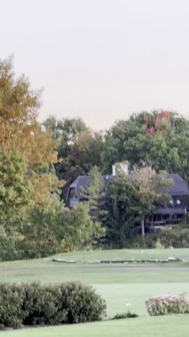 
Cozy wooden cabin nestled among tall trees in a wide open field during autumn, with colorful fall leaves changing to shades of orange, red, and yellow, sunlight filtering through branches.