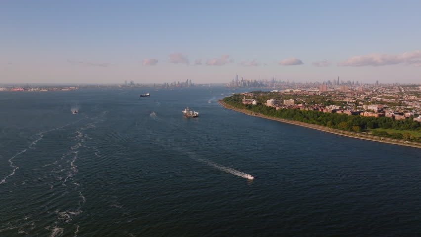 Drone aerial view of the Kill Van Kull waterway with Staten Island and Bayonne shorelines, industrial ports, and distant Manhattan skyline. Maritime shipping route on a clear sunny summer day. ProRes.