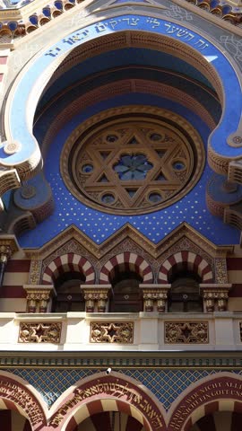Vertical screen ornate synagogue facade with Star of David intricate arches Hebrew inscriptions and golden decorations against vivid blue background showcasing rich cultural heritage and architectural