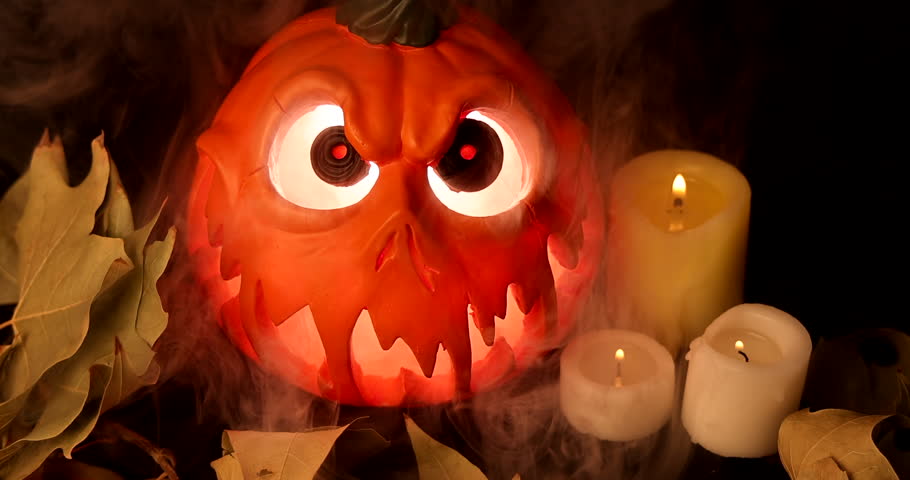 Creepy carved pumpkin shining with inner glow, mist rising, dry foliage on black Halloween surface.