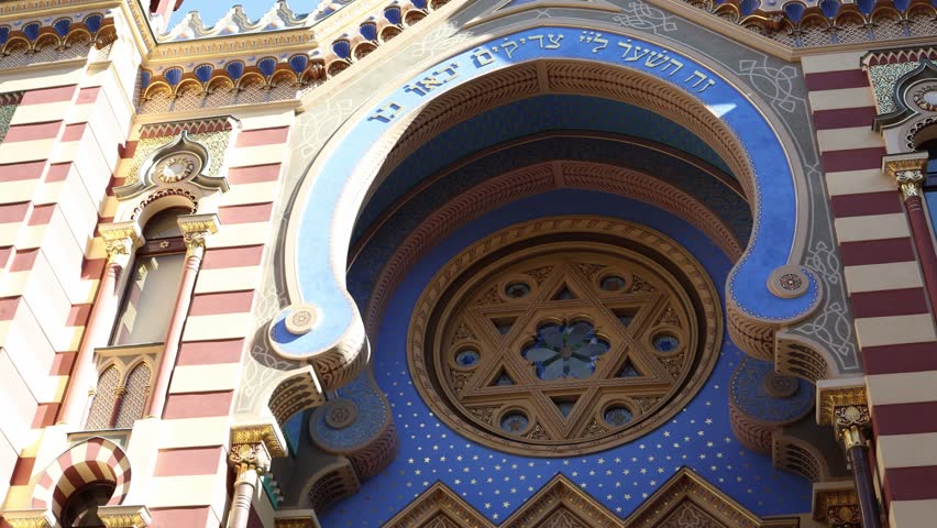 Ornate synagogue facade with detailed geometric patterns golden decorations and bright blue arch featuring Star of David and Hebrew inscriptions reflecting cultural heritage and spiritual architecture