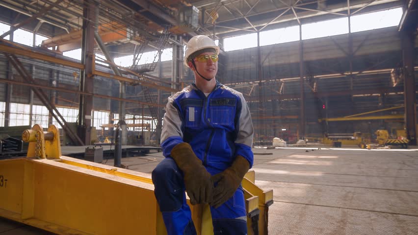 Male worker in industrial shipyard with protective gear and machinery.