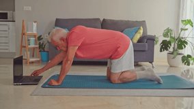 Senior man doing plank exercise at home while following online tutorial on laptop - Powered by Shutterstock - Get 15% off with code: PIKWIZARD15