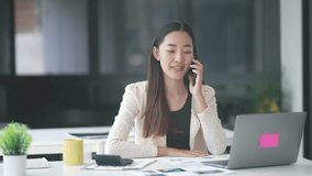 Professional Asian businesswoman working at office desk, communicating on phone with laptop and calculator, expressing cheerful confidence during business interaction - Powered by Shutterstock - Get 15% off with code: PIKWIZARD15