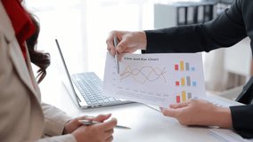 Businesswomen in formal wear discussing company performance, analyzing line graphs and bar charts, pointing with a pen, sitting at a table with a laptop - Powered by Shutterstock - Get 15% off with code: PIKWIZARD15