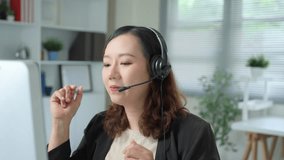 Friendly asian operator woman working in office, she is wearing headset and speaking through microphone, she is smiling and looking at computer screen - Powered by Shutterstock - Get 15% off with code: PIKWIZARD15