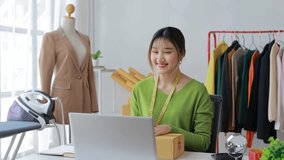Young asian fashion designer holding a package and talking to clients online using her laptop in her workshop, she is wearing a green sweater and a measuring tape - Powered by Shutterstock - Get 15% off with code: PIKWIZARD15
