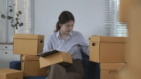 Confident young asian entrepreneur managing online business operations. Carefully checking orders and preparing shipment packages within organized home office workspace surrounded by cardboard boxes - Powered by Shutterstock - Get 15% off with code: PIKWIZARD15