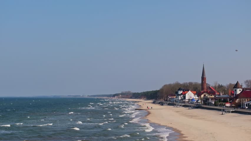 Sarbinowo’s coastline shines in March: wide sandy beach, tranquil sea, promenade, and the timeless red-brick church at the village center.