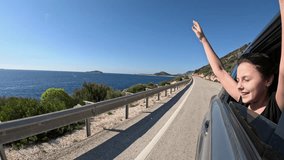 Young girl enjoying road trip by the sea. Young female passenger stretching arms wide, feeling wind during coastal highway drive, embodying carefree summer vacation freedom and joyful road trip - Powered by Shutterstock - Get 15% off with code: PIKWIZARD15