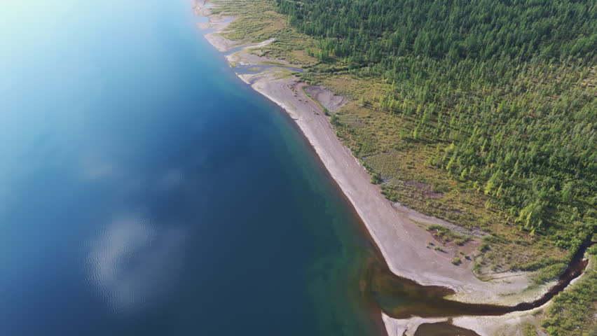 Aerial view along Lake Lama bay on the Putorana Plateau at calm evening, showing river mouth, camp and layered shoreline. Soft light, wide water and deep wilderness convey scale and travel appeal