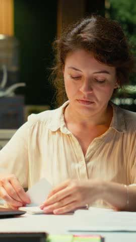 Vertical Video Livid businesswoman breaking a paper page after making a mistake, handwriting and notetaking in office after hours. Displeased impatient worker redoing the draft on a new sheet. Camera